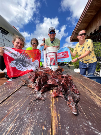 Group of lionfish hunters in Aruba holding Lionfish University flag. with the lionfish catch of the day on table.