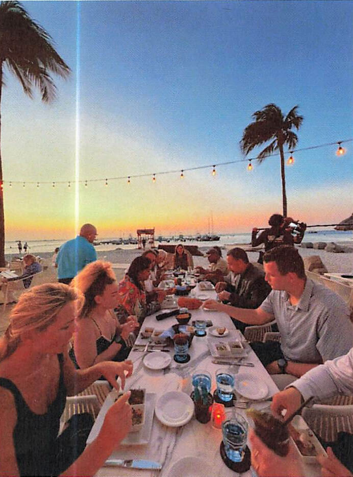 Guests dining beachside at sunset while cameras roll
